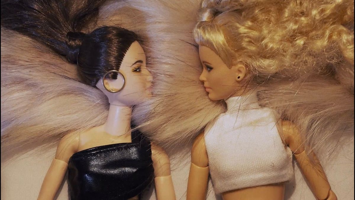 still from the kill 2 video: two fashion dolls lying on white fur